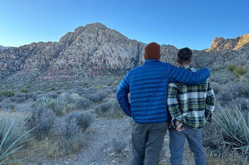 Two people walking on a dirt path with a mountainous landscape in the background. 2