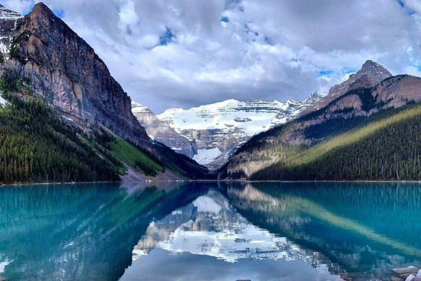 A mountain lake with reflections, surrounded by forested mountains and snow-capped peaks. 1