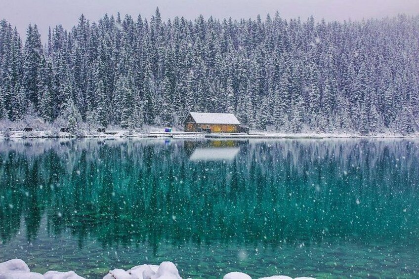 Une cabane au bord d’un lac enneigé, dont les eaux reflètent les arbres. 2