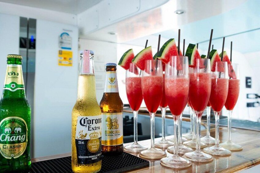 Un bar con botellas de cerveza y vasos de una bebida roja, posiblemente un cóctel, con trozos de sandía. 3