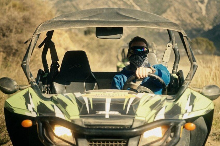 A person driving a green off-road vehicle with a clear windshield and a visible dashboard. 2