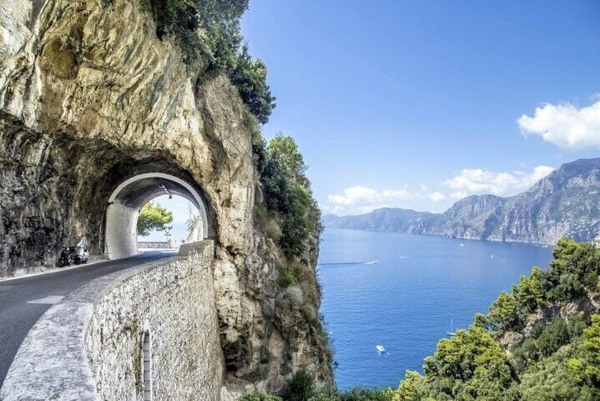 A coastal road tunnel with a view of the sea and distant mountains. 1