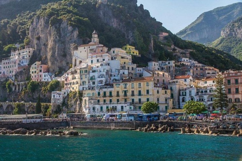 A coastal town with colorful buildings perched on a cliff, a marina with boats, and a clear blue sea. 2