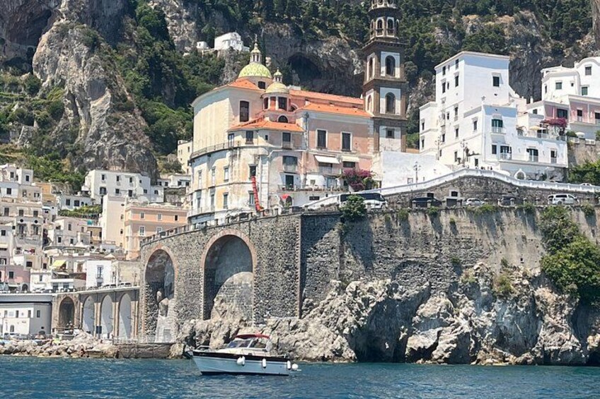 A coastal town with a prominent stone bridge, buildings with colorful facades, and a boat on the water. 5