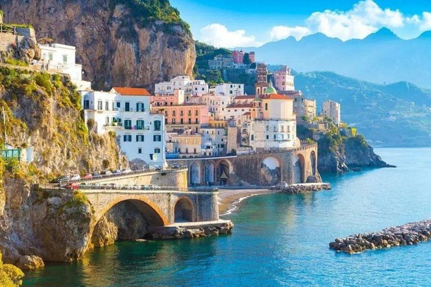 A coastal town with colorful buildings, a stone bridge, and a clear blue sea. 3