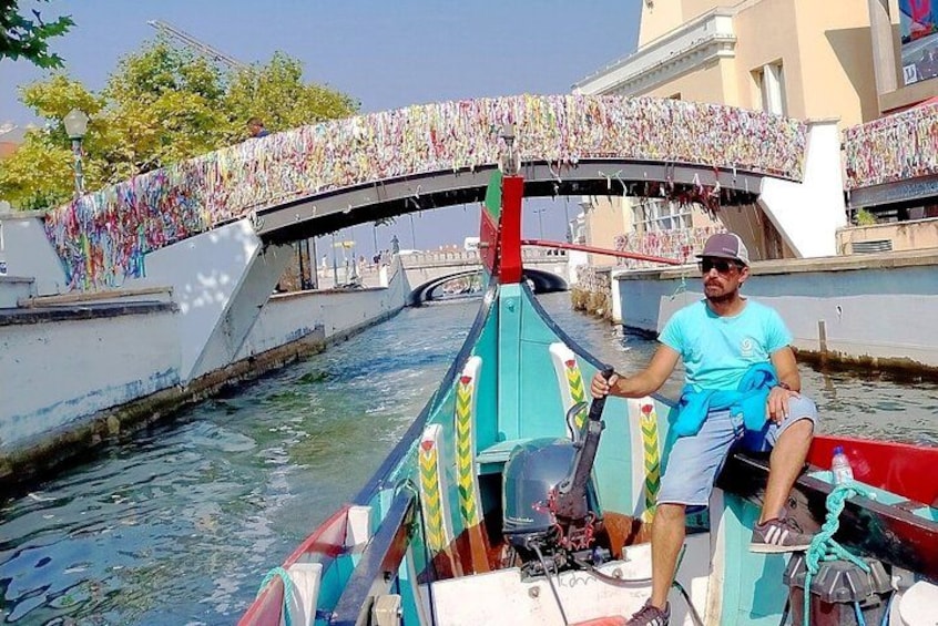 A man on a colorful boat with a bridge in the background. 3