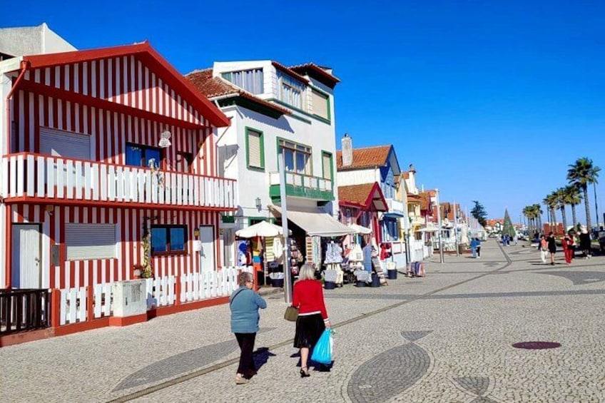 A cobblestone street lined with colorful buildings, palm trees, and people walking. 4