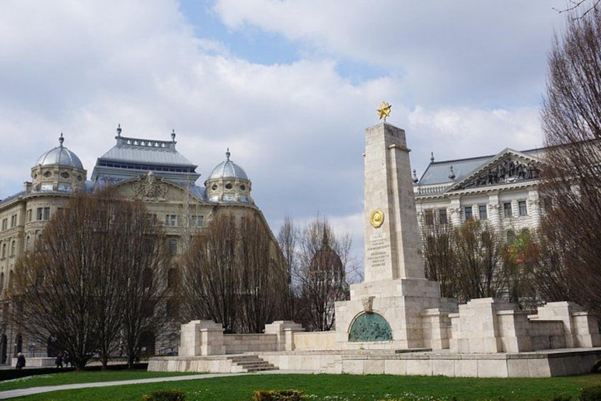 A monument with a statue, surrounded by trees and buildings. 3