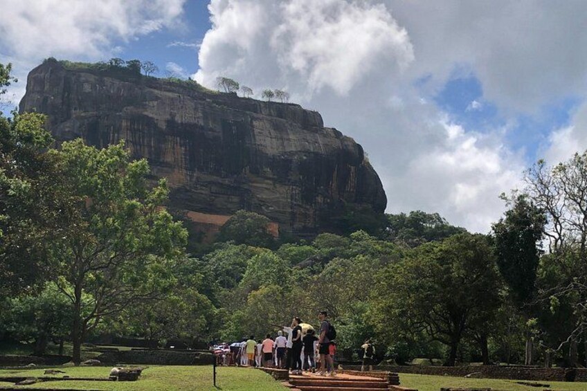 A large rock formation, a grassy area, and a group of people gathered near a structure. 3