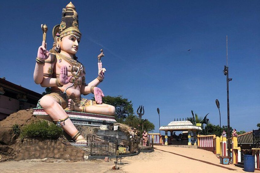 A large statue of a deity with multiple arms, a large rock formation, and a pathway leading to a building. 2