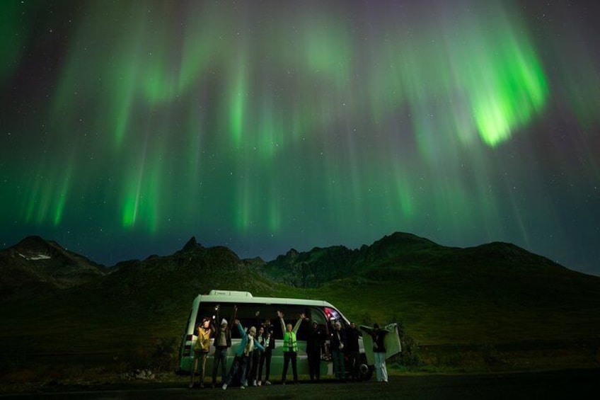 A group of people standing in front of a vehicle under the Northern Lights. 4