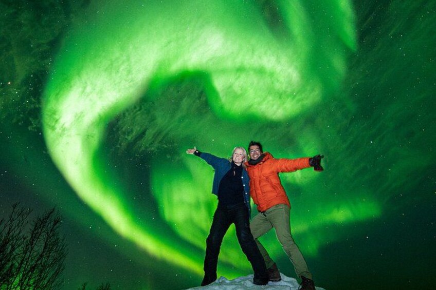 To personer står i sneen med et grønt nordlys i baggrunden. 1