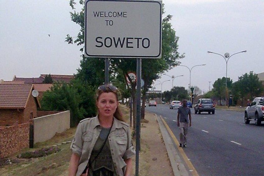 A welcome sign to Sowejo, a person walking on the sidewalk, and a street with cars. 5
