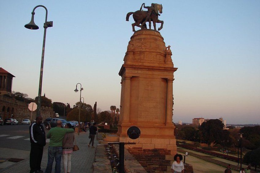 A monument with a horse statue, surrounded by people and urban buildings. 2
