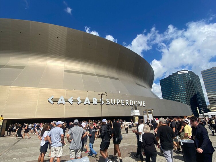 A large, curved building with 'CAESARS SUPERDOME' written on its facade, surrounded by a crowd of people. 5
