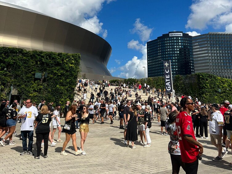 A crowded outdoor area with a large curved building and a staircase leading to a higher platform. 3
