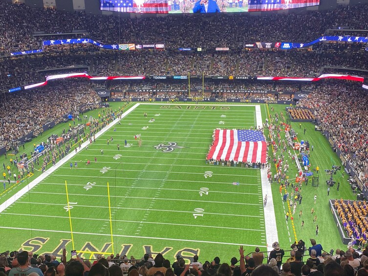 A football stadium with a large American flag on the field, surrounded by spectators. 4