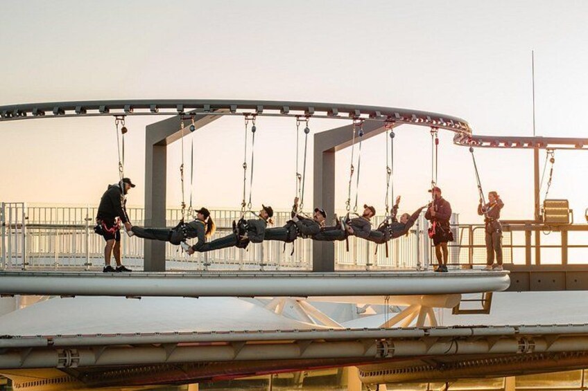 A swing ride with people seated and swinging, a metal structure, and a railing. 2