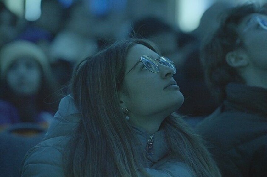 A person wearing glasses and a jacket, with a blurred background of other people. 3
