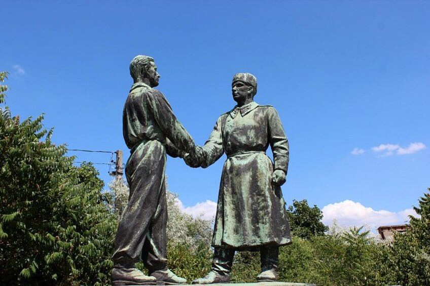 En statue af to personer, der giver hinanden hånden, omgivet af grønt og en klar himmel. 4