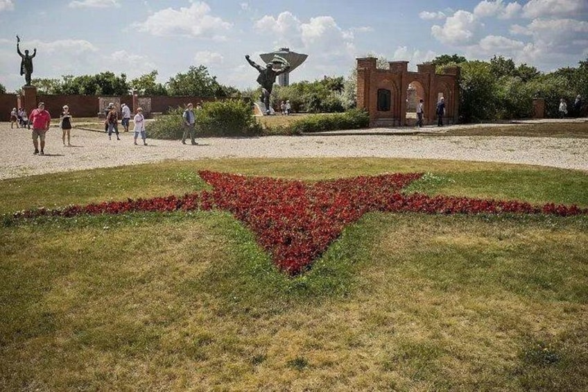 En anlagt have med et blomsterbed i rødt, en statue og en murstruktur. 3