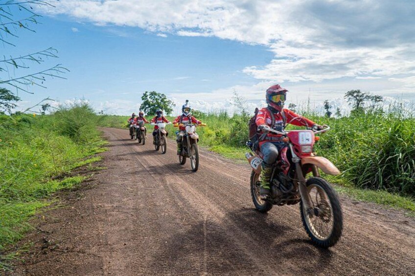 A group of motorcyclists on a dirt road surrounded by greenery. 1