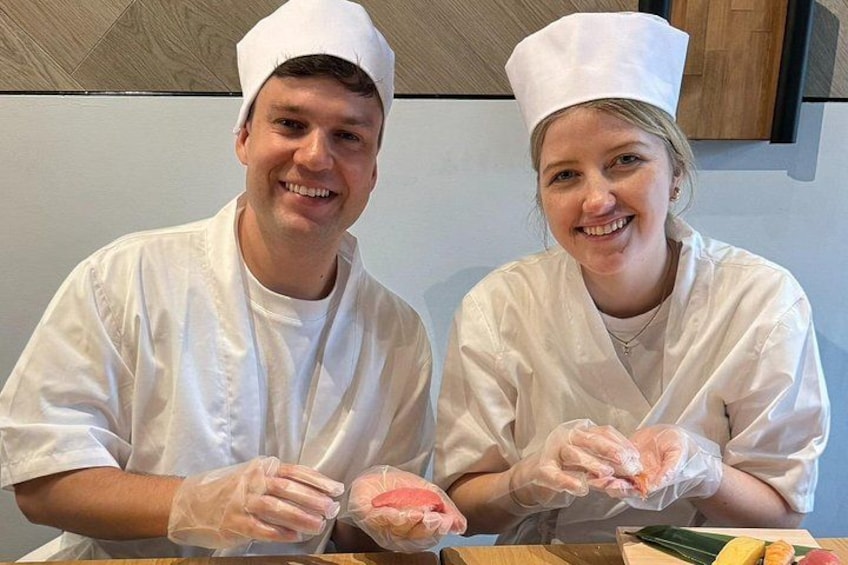 Dos cocineros con uniformes y gorros blancos sostienen un objeto rosa, posiblemente comida, en una cocina. 3
