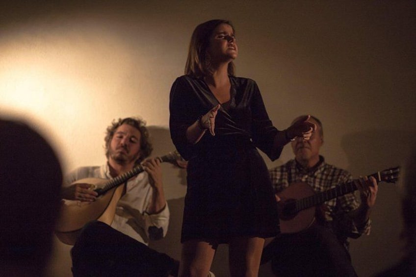 A person playing a guitar, another person singing, and a third person playing a guitar in a dimly lit room. 1