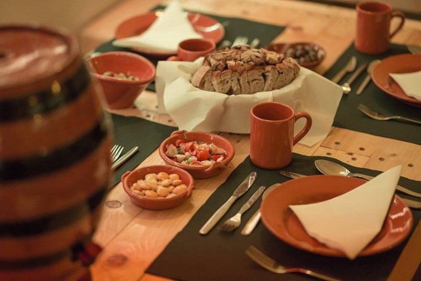 A wooden table with a meal setup including bowls of beans, a loaf of bread, and a mug. 2