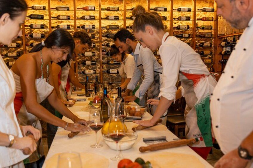 A group of people preparing food in a kitchen with wine bottles in the background. 4