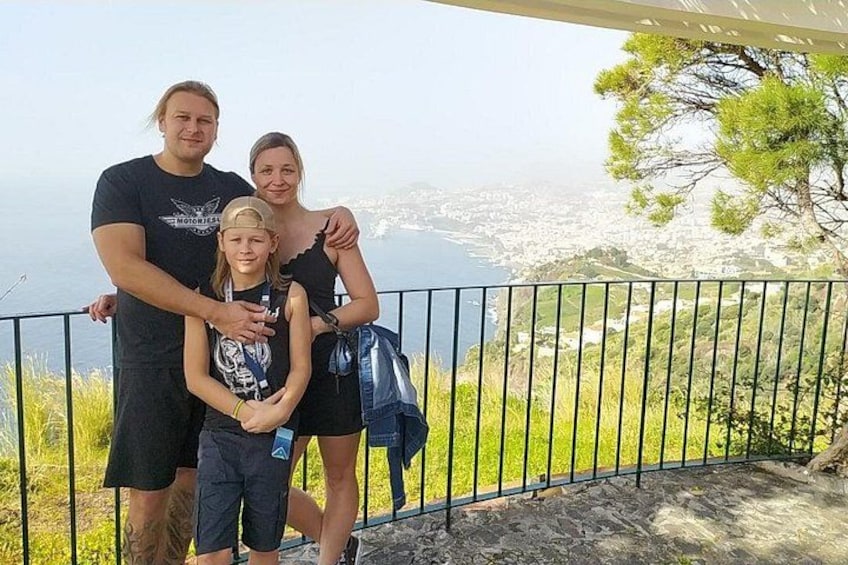 Une famille de trois personnes se tient sur un balcon, avec une vue sur la ville en arrière-plan. 2