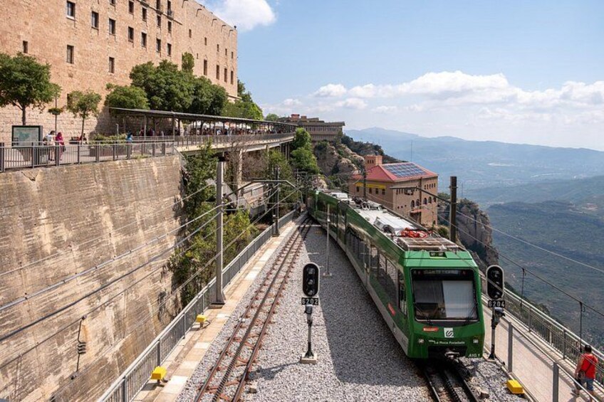 Un train vert sur une pente abrupte, un mur de pierre et un bâtiment avec un toit rouge. 5