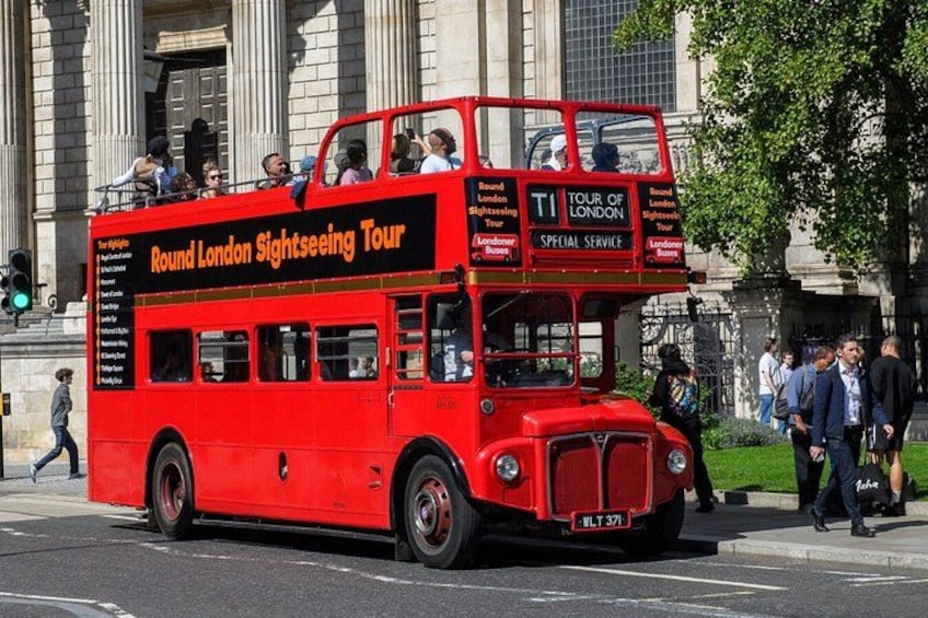 A red double-decker bus labeled 'Round London Sightseeing Tour' on a city street. 1