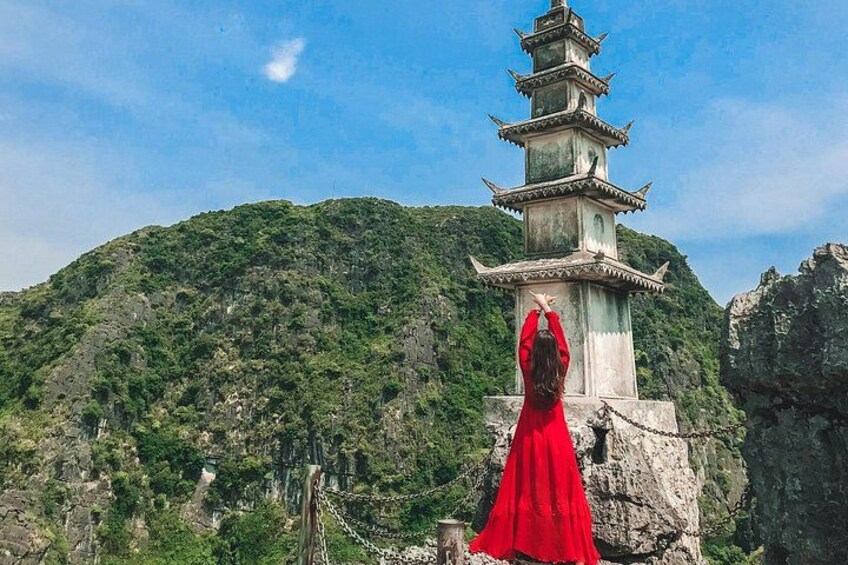 A person in a red dress standing in front of a traditional multi-tiered pagoda with a mountainous backdrop. 1