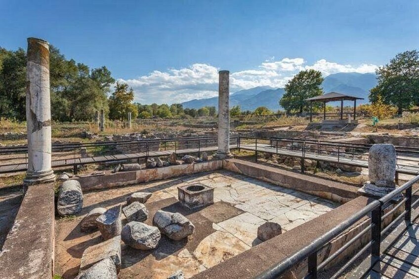 Rovine antiche con colonne in pietra e una vasca di pietra, circondate da una ringhiera metallica. 4