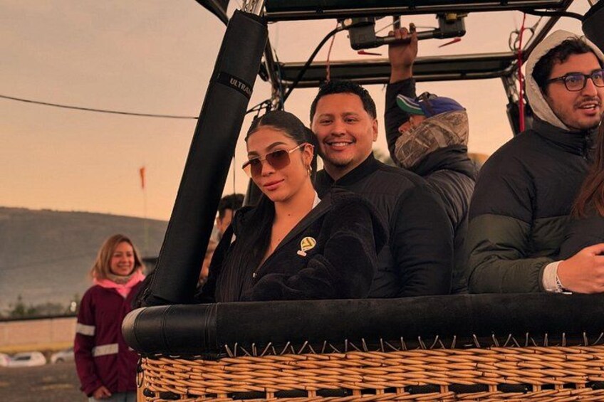 A group of people in a wicker basket on a vehicle, with a hilly landscape in the background. 2