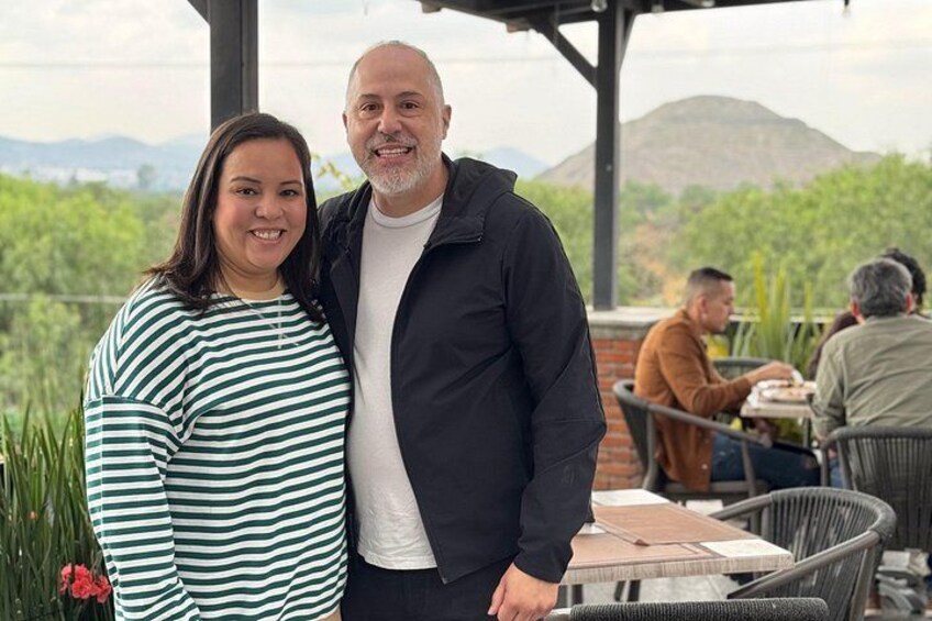 Two people standing outdoors with a mountainous landscape in the background. 5