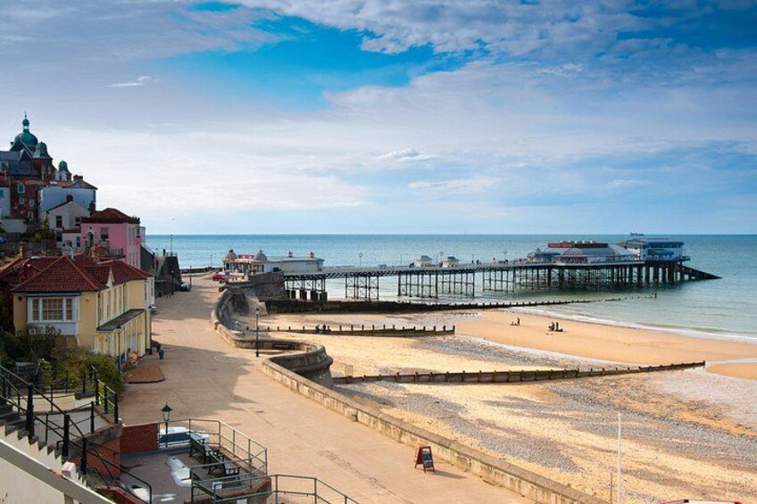 A beach with a pier extending into the sea, buildings in the background, and a clear sky. 1