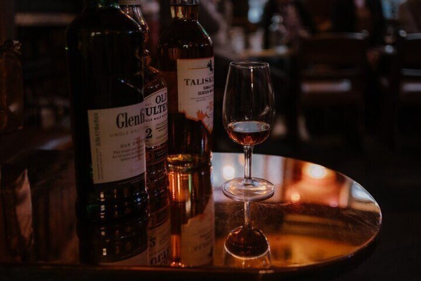 A bottle of Glenfiddich whisky and a glass of whisky on a reflective surface. 2