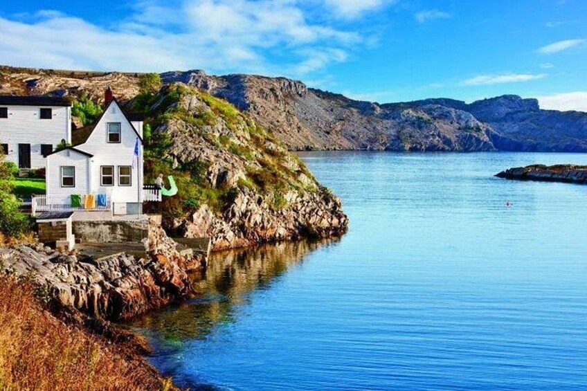 A white house by a calm sea with rocky cliffs in the background. 1