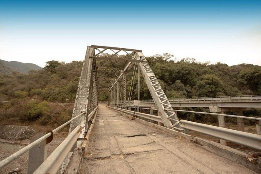 Un puente de metal con estructura de celosía, rodeado por un paisaje montañoso con vegetación escasa. 4