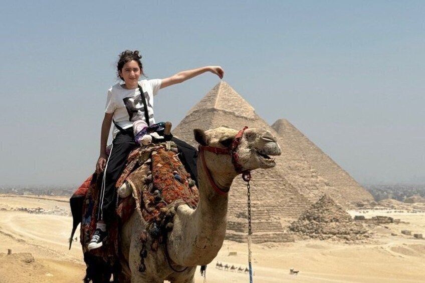 Een persoon die op een kameel rijdt, met een piramide op de achtergrond. 4
