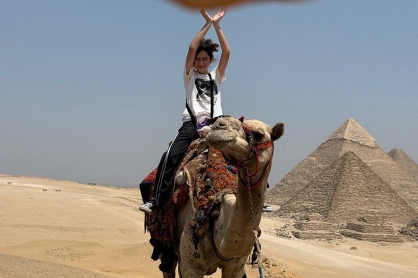 Een persoon die op een kameel rijdt, met een piramide op de achtergrond. 3