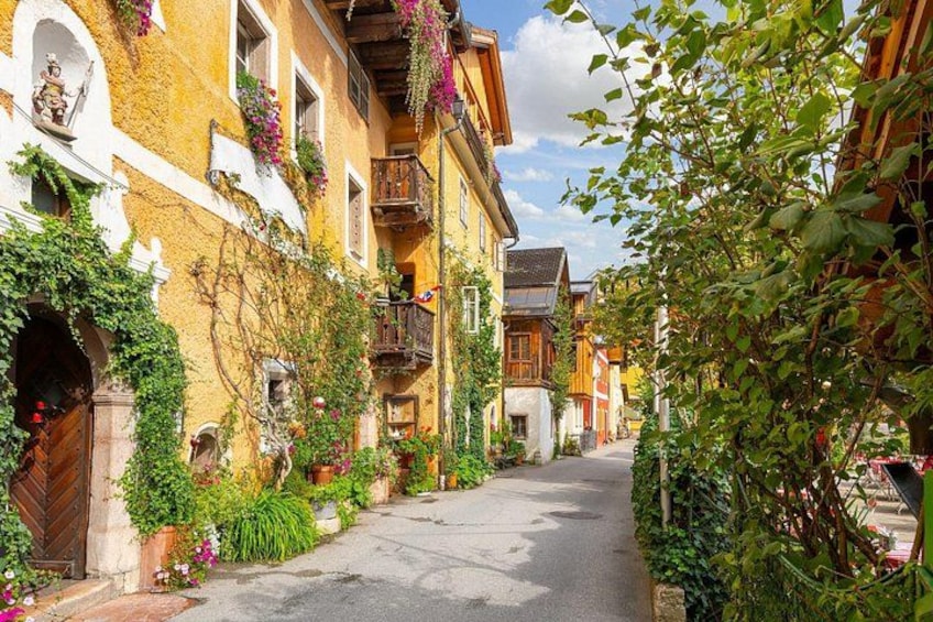A narrow street lined with colorful buildings, some with balconies adorned with flowers. 2