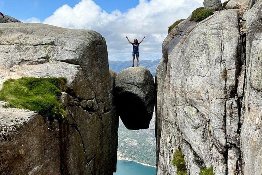 A person standing on a rock formation with arms raised, overlooking a valley. 1