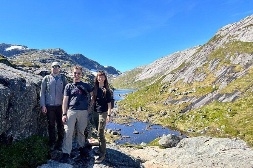 Three people standing on a rocky terrain with a lake and mountains in the background. 2