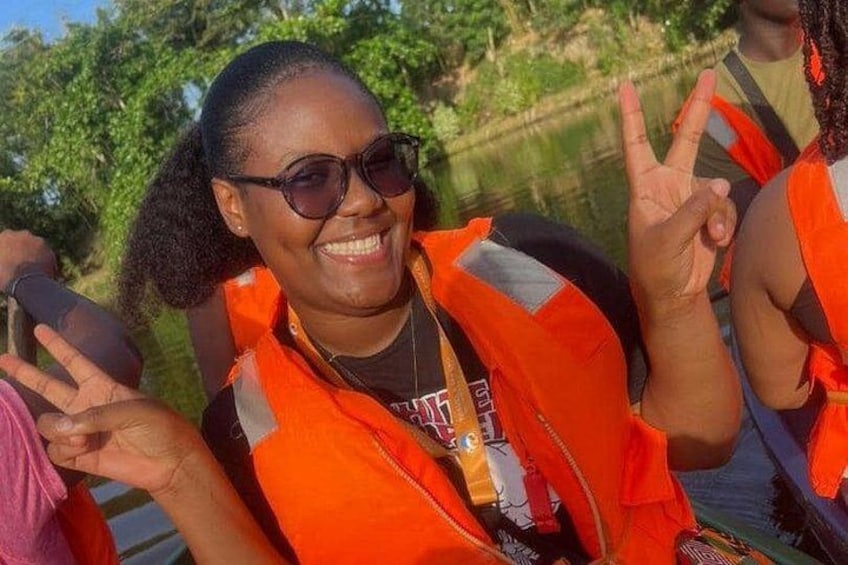 A person wearing an orange life jacket, holding a camera, and making a peace sign. 2