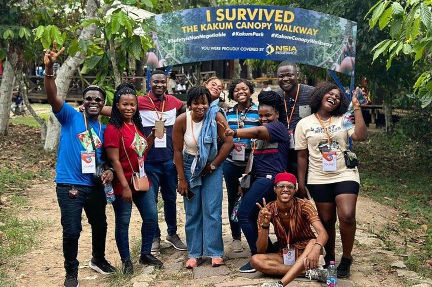 A group of people posing in front of a sign that reads 'I Survived The Kakum Canopy Walkway.' 5