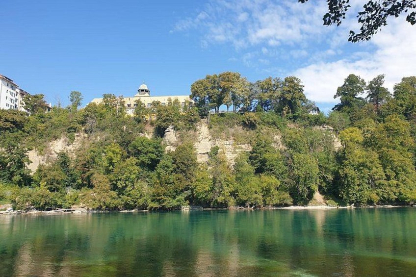A calm lake with a rocky cliff and a building on top. 5