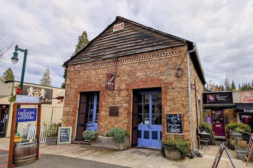 A stone building with a blue door and windows, surrounded by potted plants and a signboard. 4